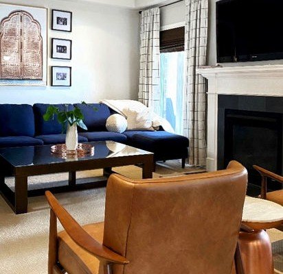 After: the same room with a navy sectional, a carved arched panel and black-and-white photographs on the wall, and two tan leather chairs.