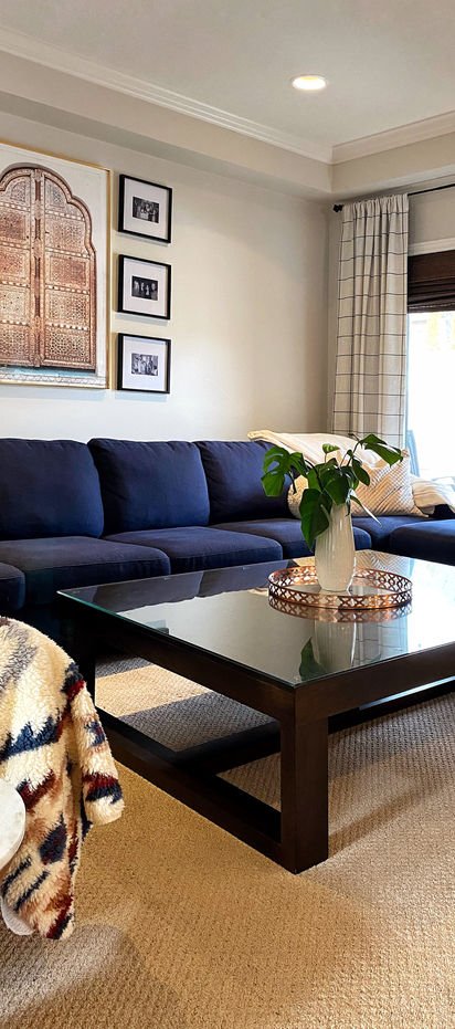 A carved arched panel from India above a navy sectional, beside three black-and-white family photographs.