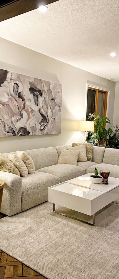 A cream boucle sectional under a large soft abstract canvas, with a white lacquer coffee table.