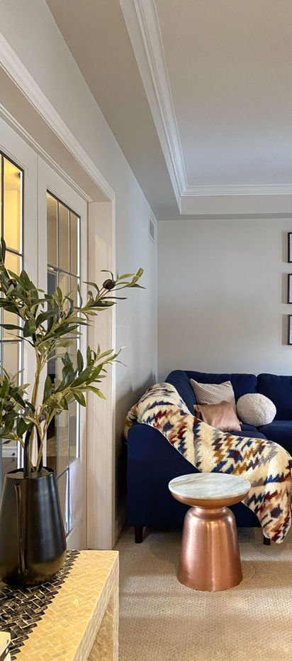 A navy sofa with a woven kilim throw, a hammered copper drum side table and olive branches in a tall black vase.