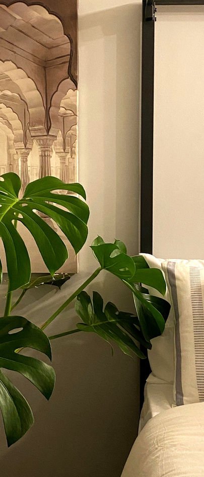 A drawing of a receding arched colonnade, in sepia, beside a bed, with monstera leaves in front of it.
