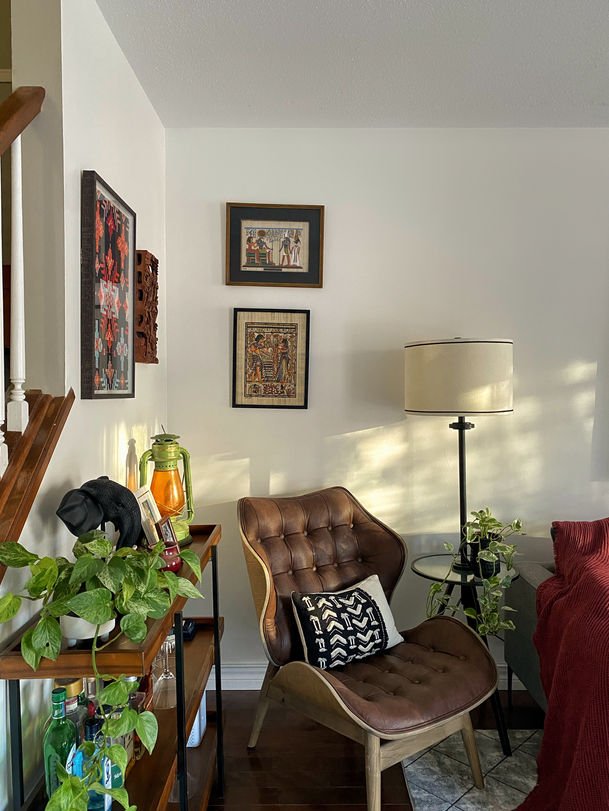 A corner holding framed papyrus, a carved wooden panel, a green lantern and a patterned cushion on a brown leather chair.